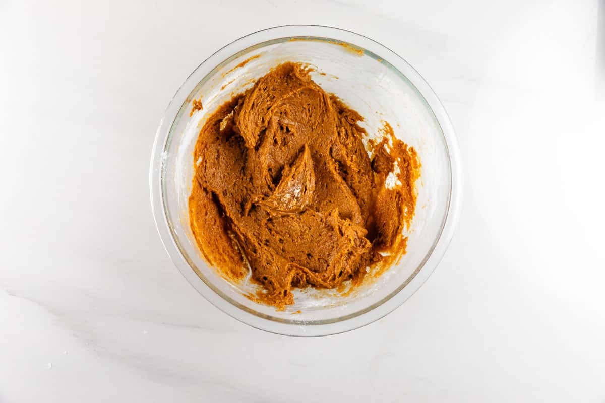 A glass bowl filled with brown cookie dough sits on a white countertop.