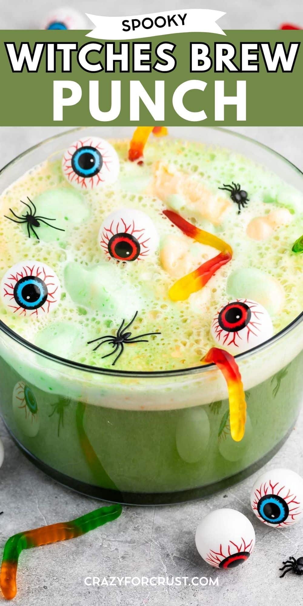 A bowl of green punch with floating gummy worms and candy eyeballs, decorated for Halloween, labeled Spooky Witches Brew Punch..