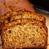 Close-up of several slices of golden-brown banana bread arranged on parchment paper, showing a soft, moist texture with a slightly crisp crust.