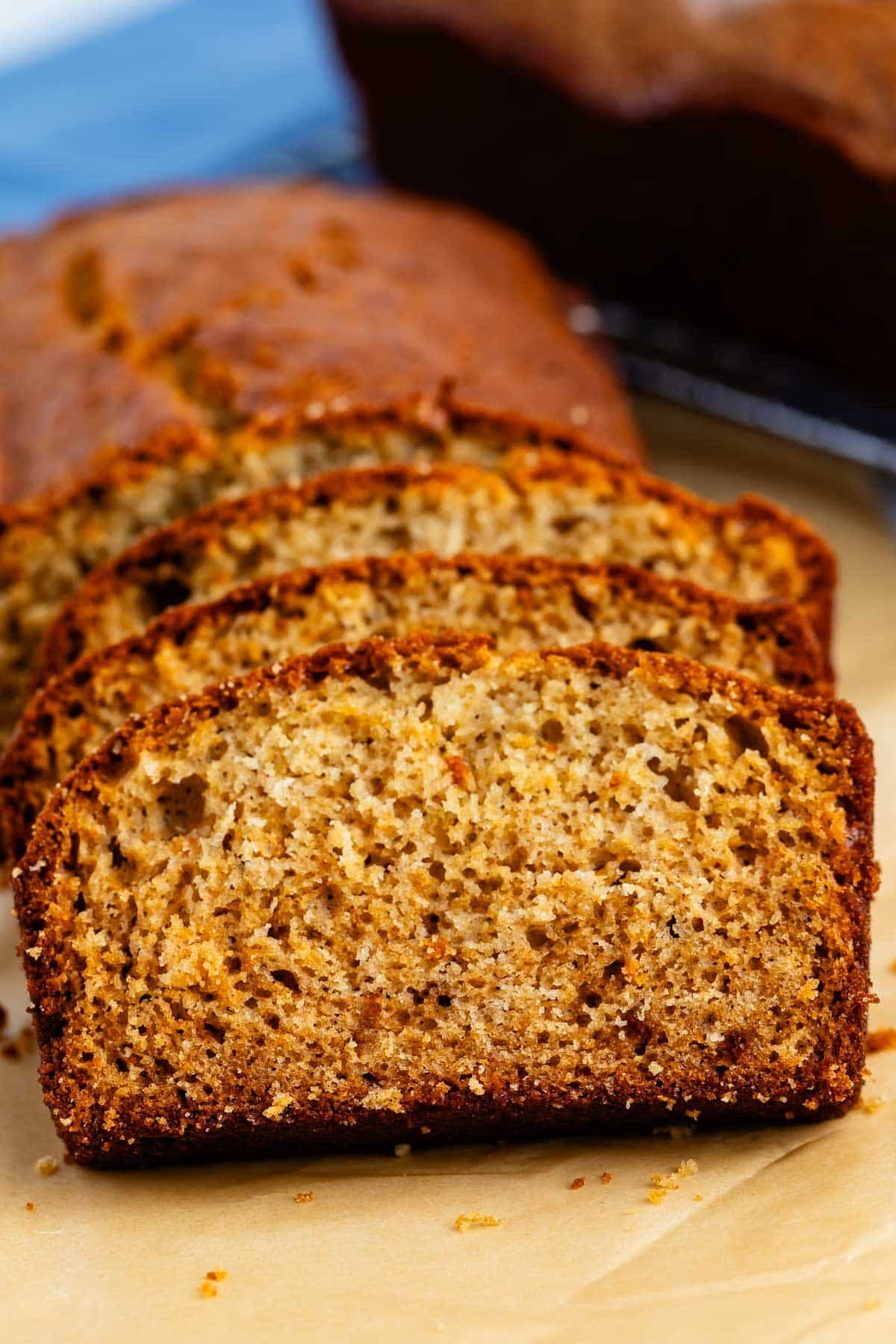 Close-up of several slices of golden-brown banana bread arranged on parchment paper, showing a soft, moist texture with a slightly crisp crust.
