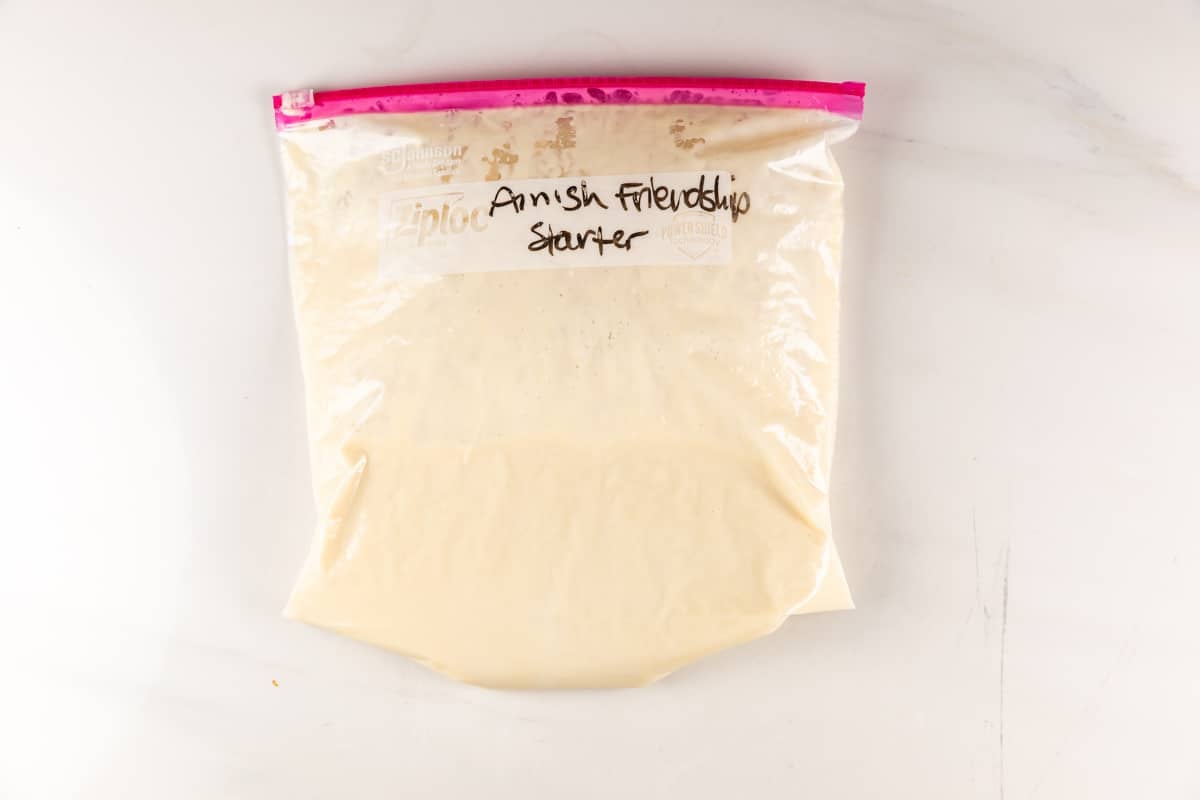 A clear zip-top bag filled with a creamy mixture labeled Amish Friendship Starter in black marker, placed on a white surface.