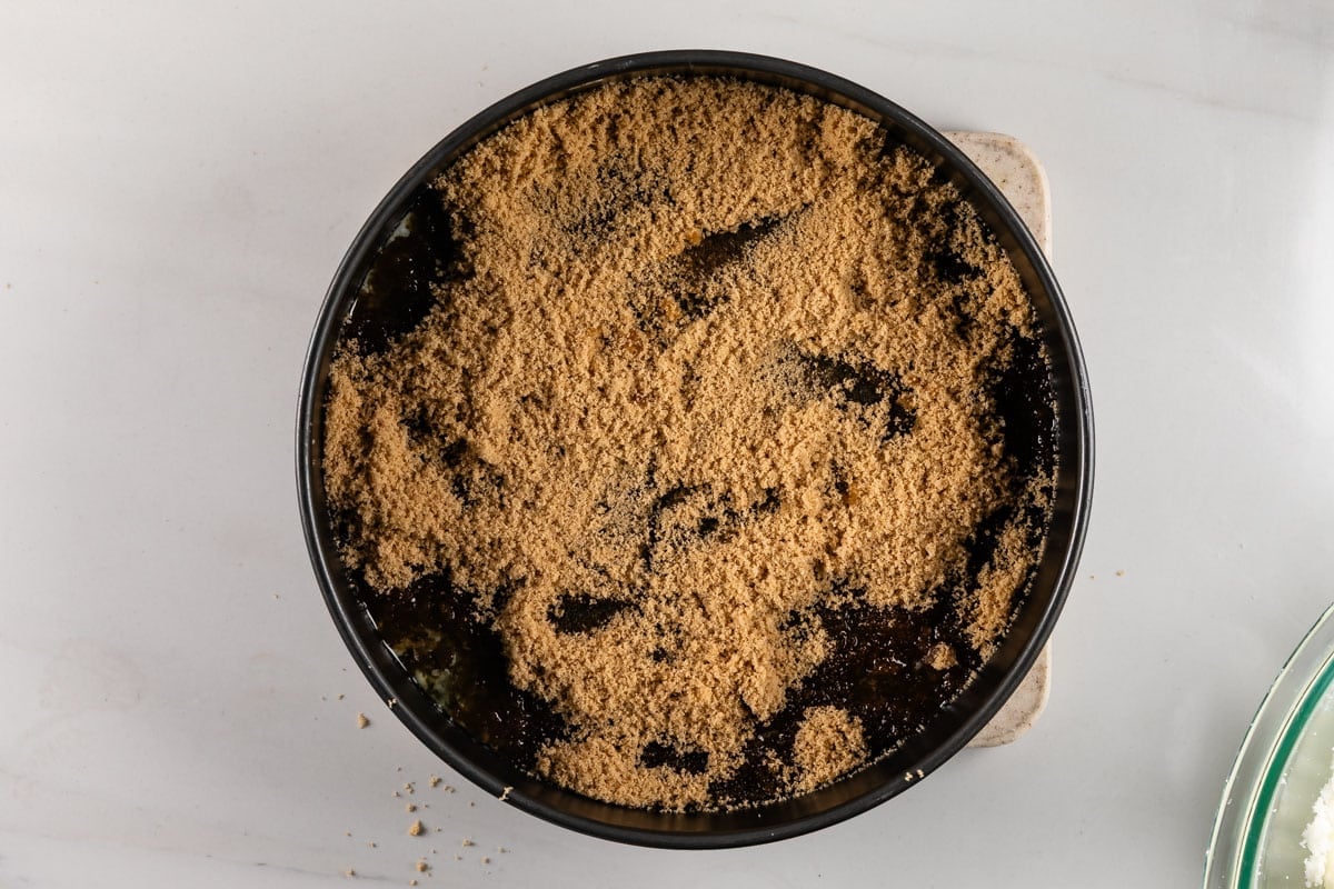 A round baking pan filled with a dark mixture topped with an even layer of brown sugar, placed on a light countertop.