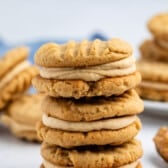 A close-up of stacked peanut butter sandwich cookies filled with creamy peanut butter frosting; more cookies are blurred in the background.