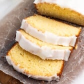 A loaf of glazed lemon pound cake sliced on a piece of parchment paper.