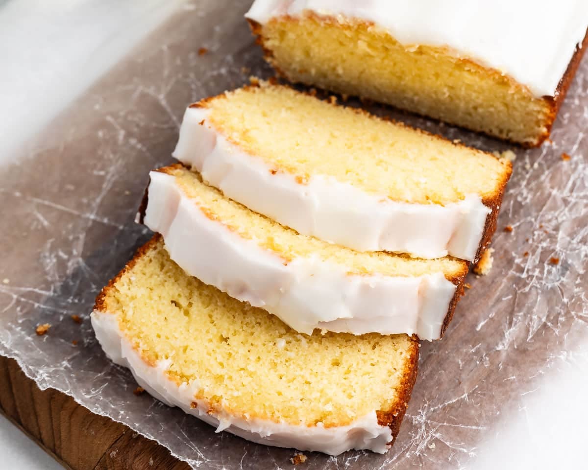 A loaf of glazed lemon pound cake sliced on a piece of parchment paper.