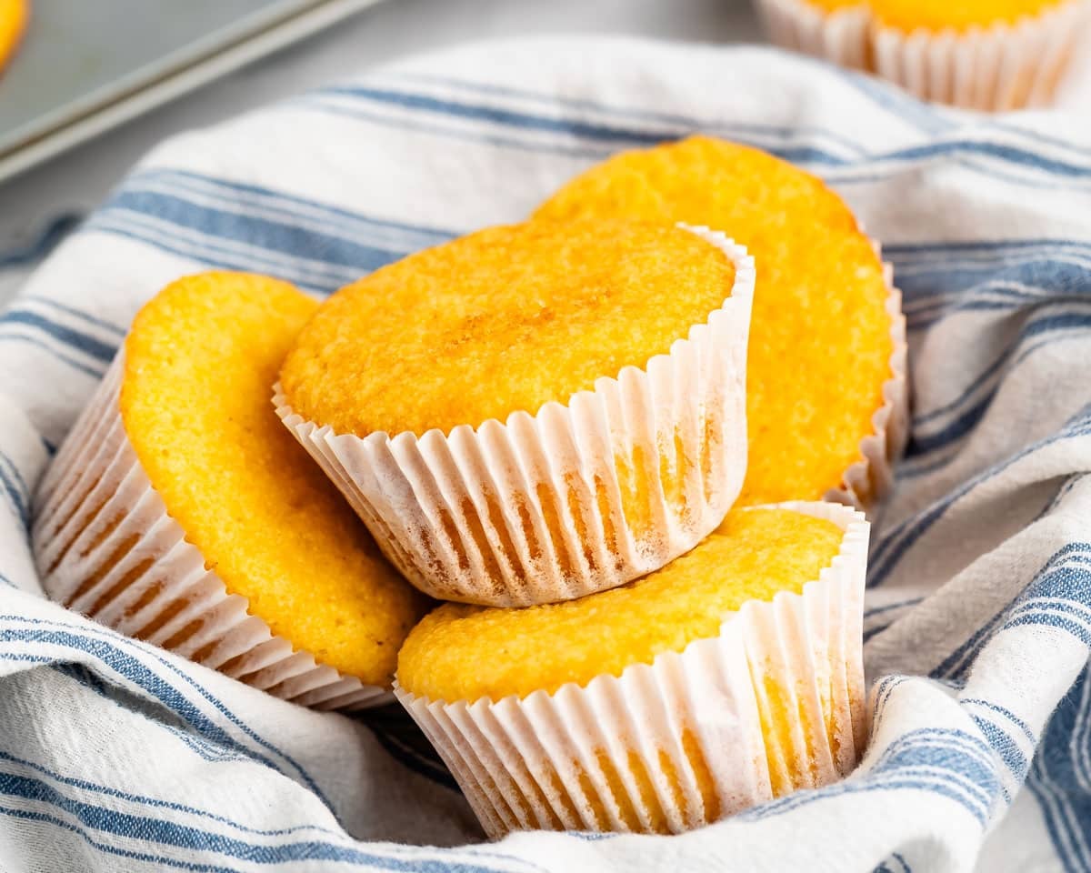Four golden-yellow corn muffins in paper liners nestled in a blue and white striped cloth.