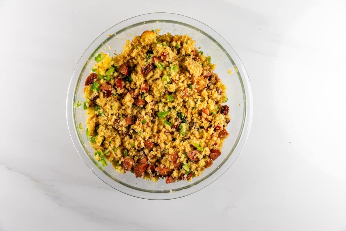 A glass bowl filled with cornbread dressing containing chopped green peppers and pieces of sausage.