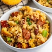 A bowl of cornbread dressing with sausage, pecans, and green peppers.