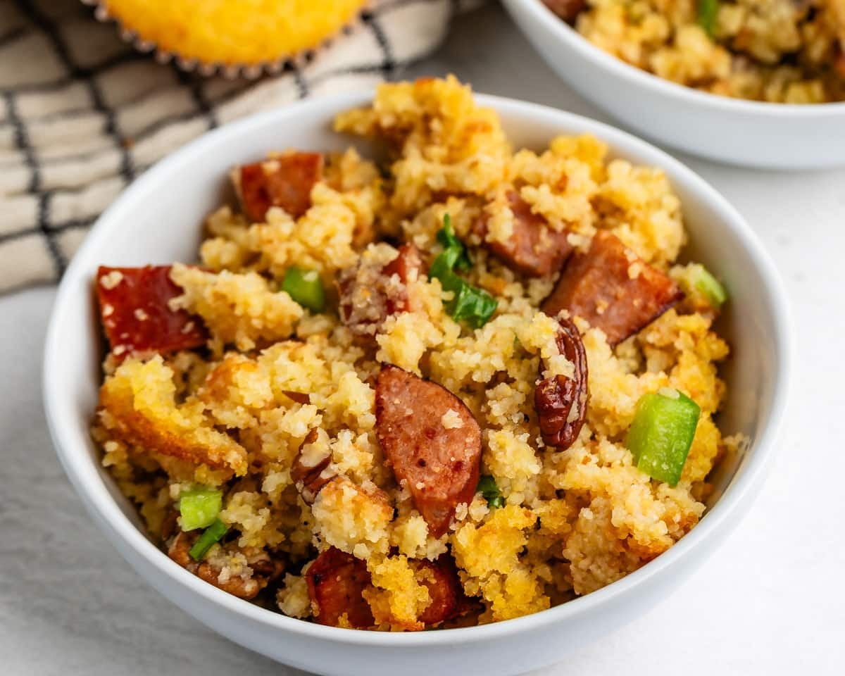 A bowl of cornbread dressing with sausage, pecans, and green peppers.