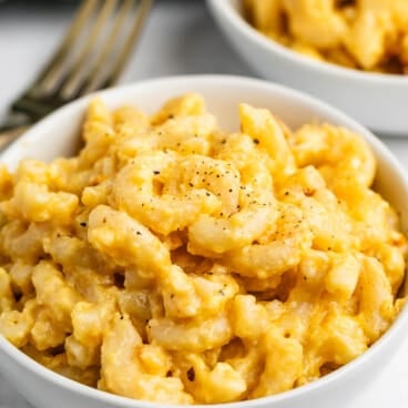Two white bowls filled with creamy macaroni and cheese, sprinkled with black pepper, with a fork nearby.