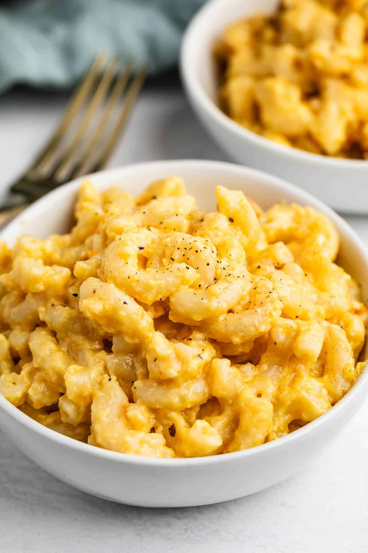 Two white bowls filled with creamy macaroni and cheese, sprinkled with black pepper, with a fork nearby.