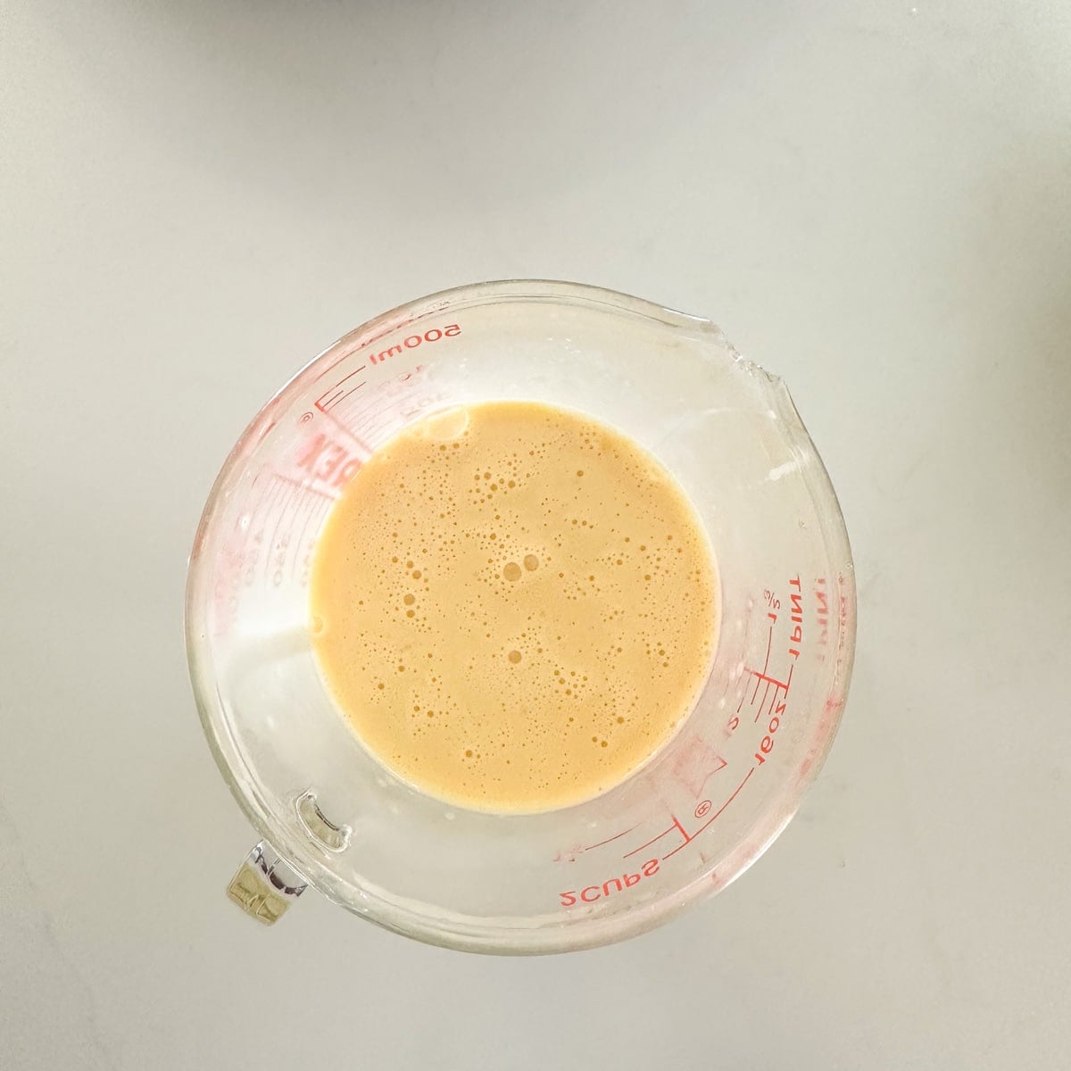 Whisked eggs in a glass measuring cup.