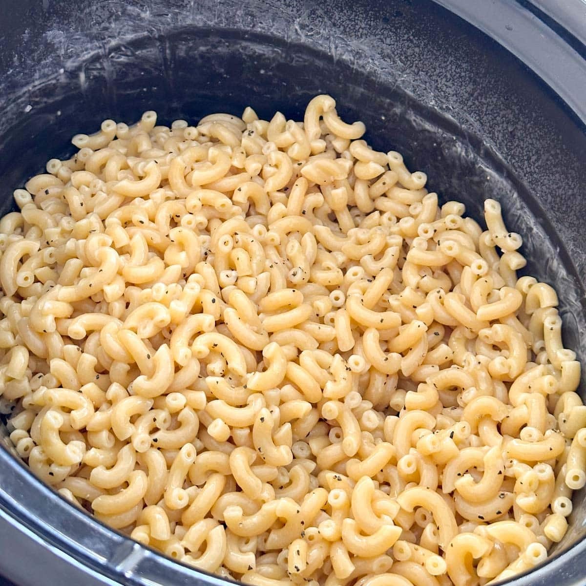 Cooked macaroni pasta tossed with black pepper in a slow cooker.