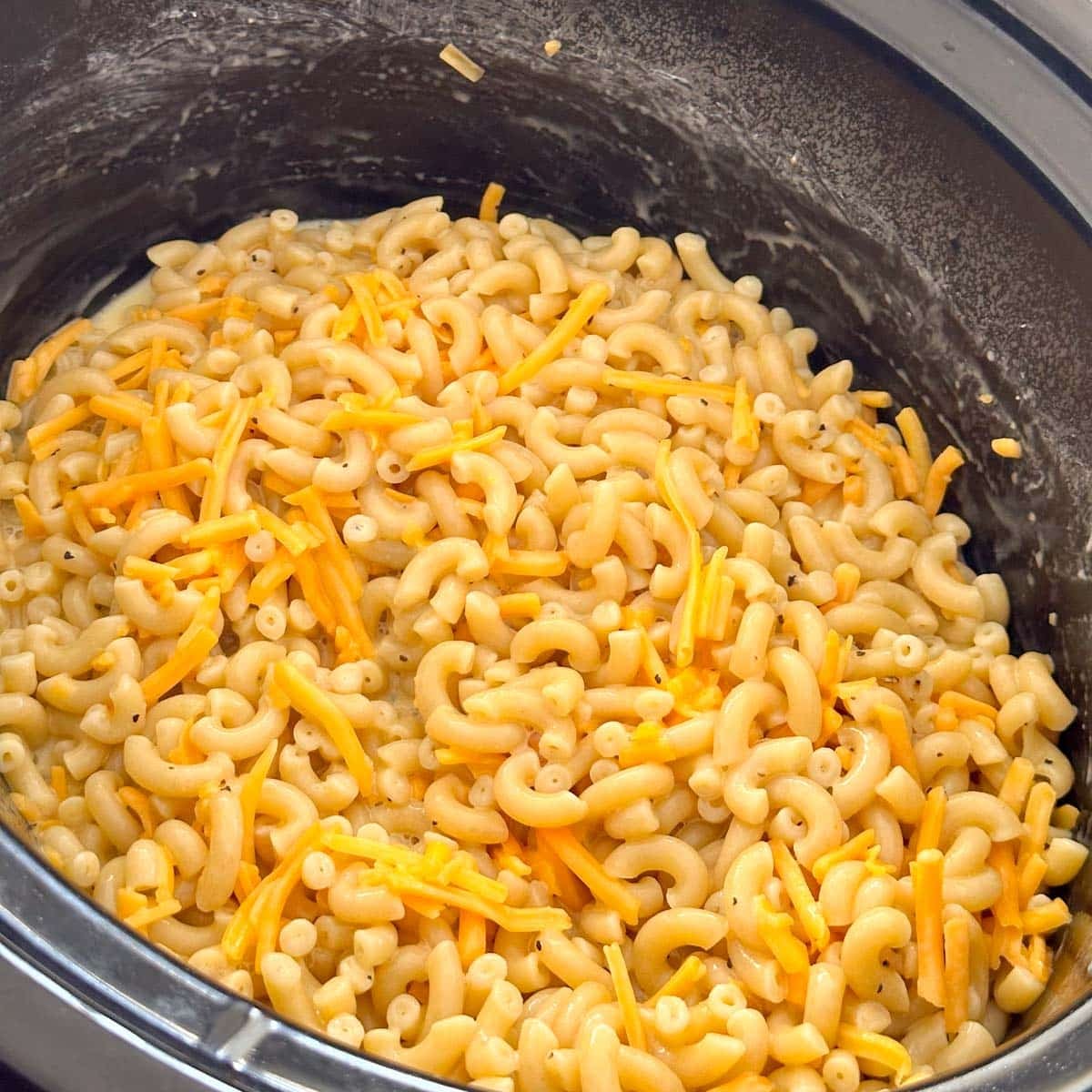 Macaroni and cheese in a slow cooker topped with shredded cheddar cheese.