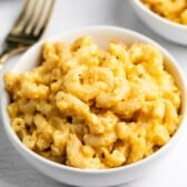 A white bowl filled with macaroni and cheese, with a gold fork nearby.