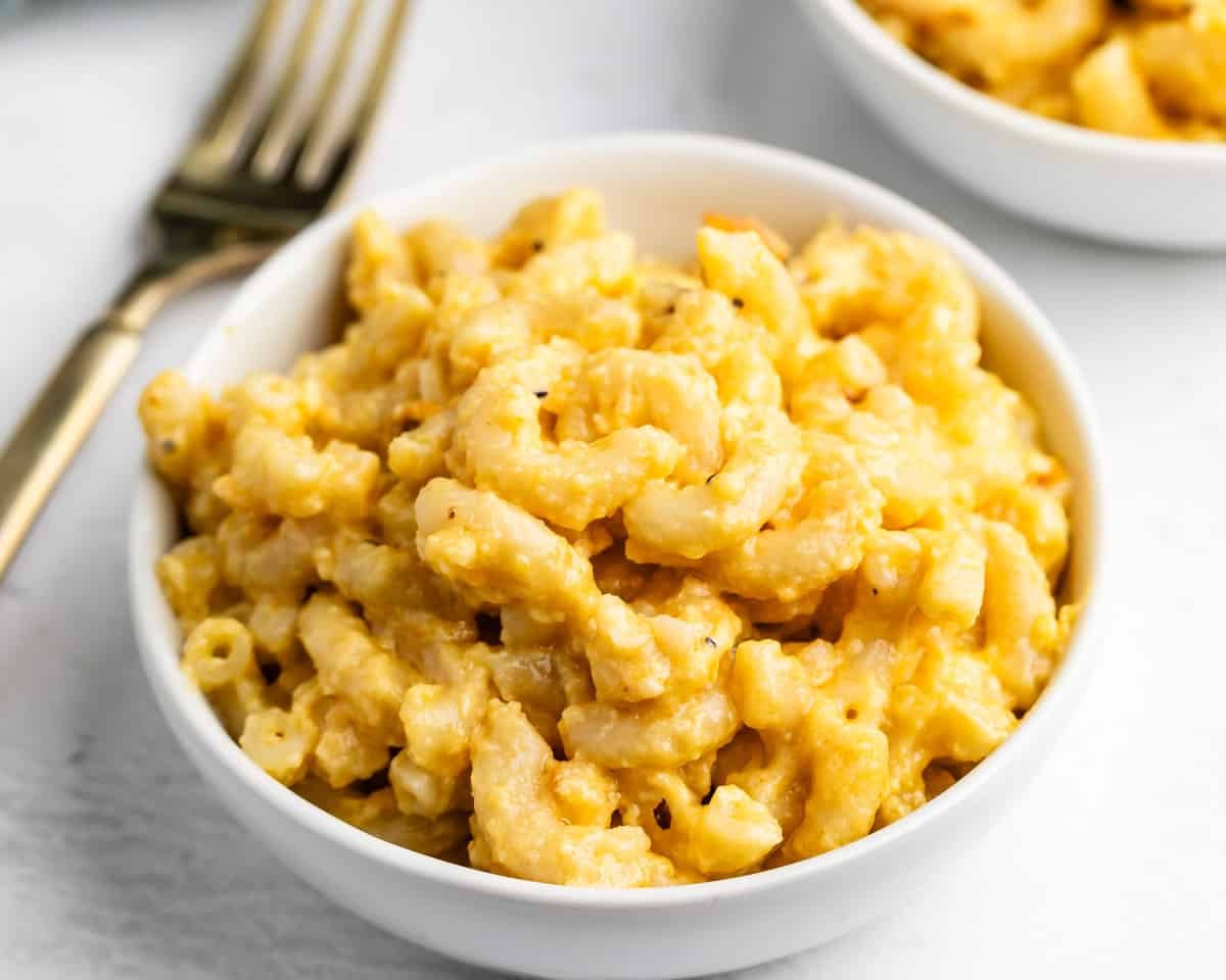 A white bowl filled with macaroni and cheese, with a gold fork nearby.