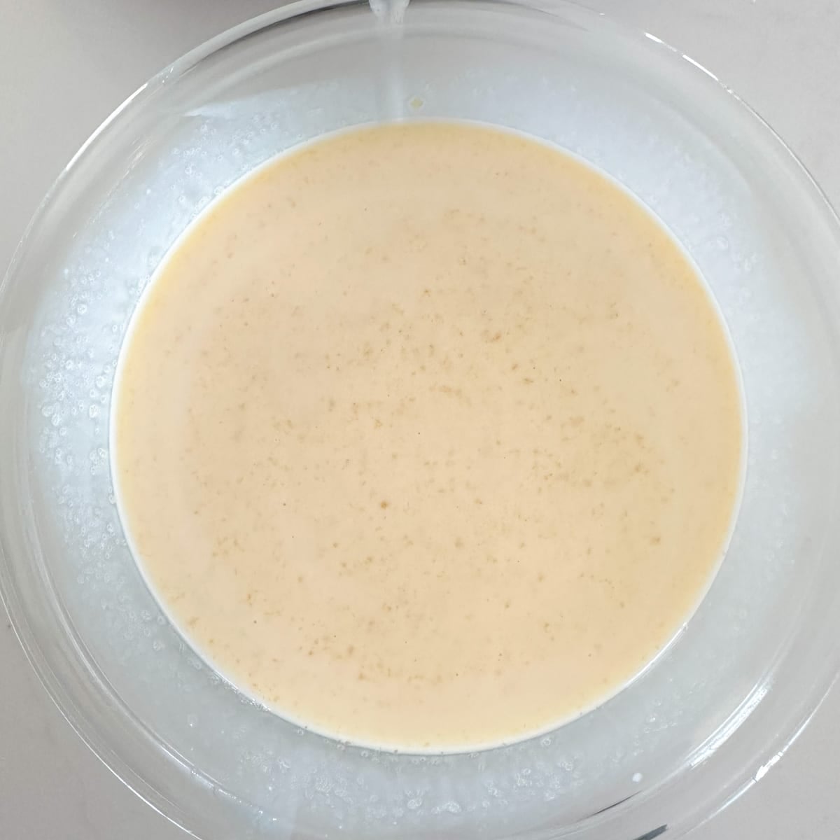 A clear glass bowl filled with a smooth, beige batter containing small flecks.
