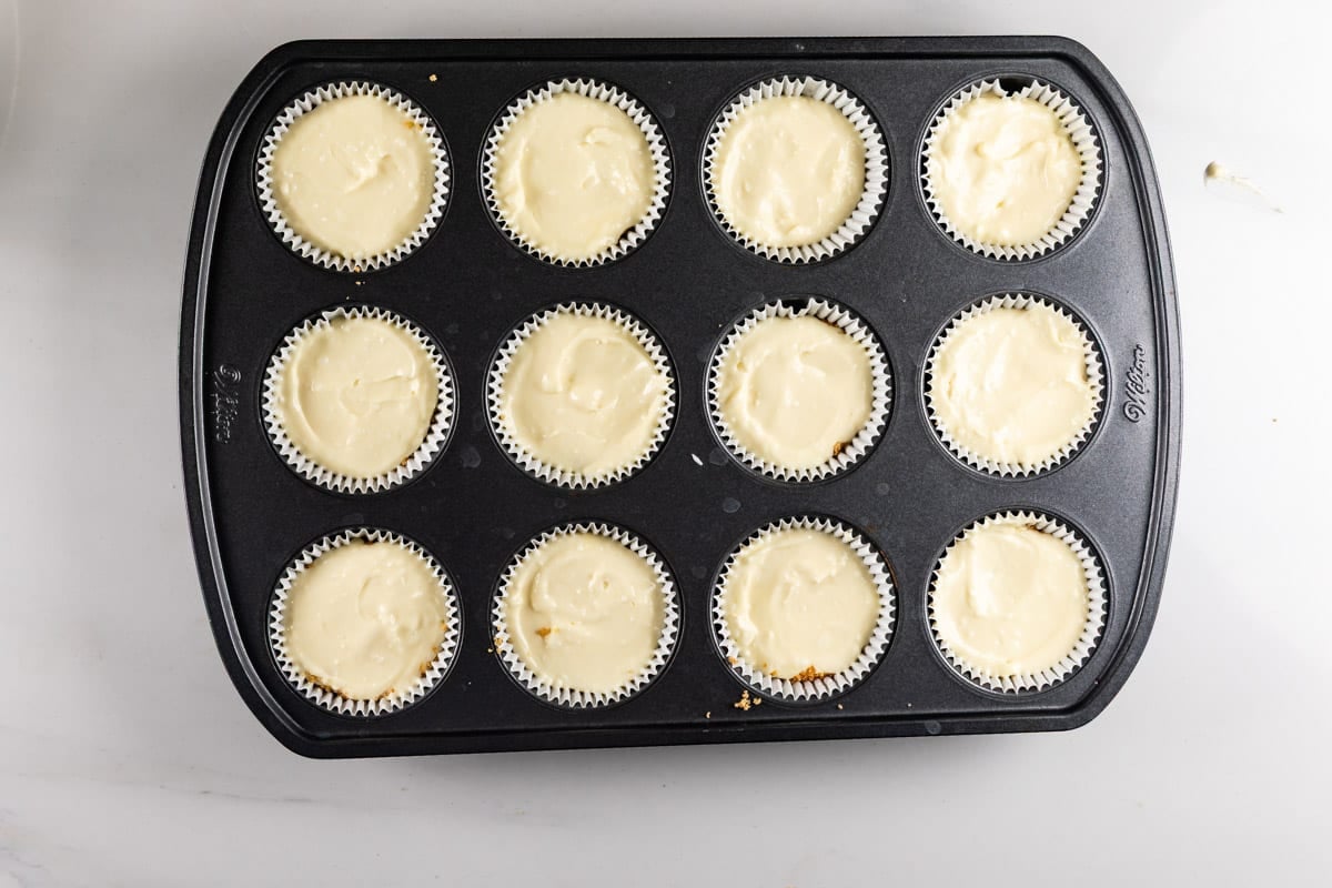 A muffin tin filled with twelve cupcake liners containing raw cake batter.