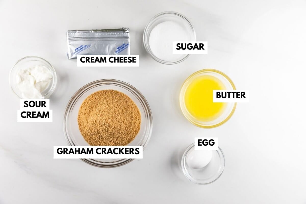 Ingredients for a recipe labeled with text: cream cheese, sugar, sour cream, graham crackers, butter, and an egg.