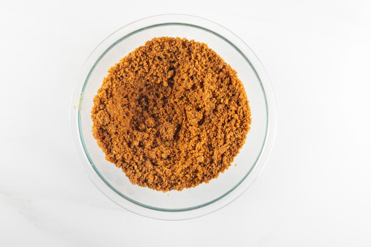 Crumbled graham cracker crust in a clear glass mixing bowl.
