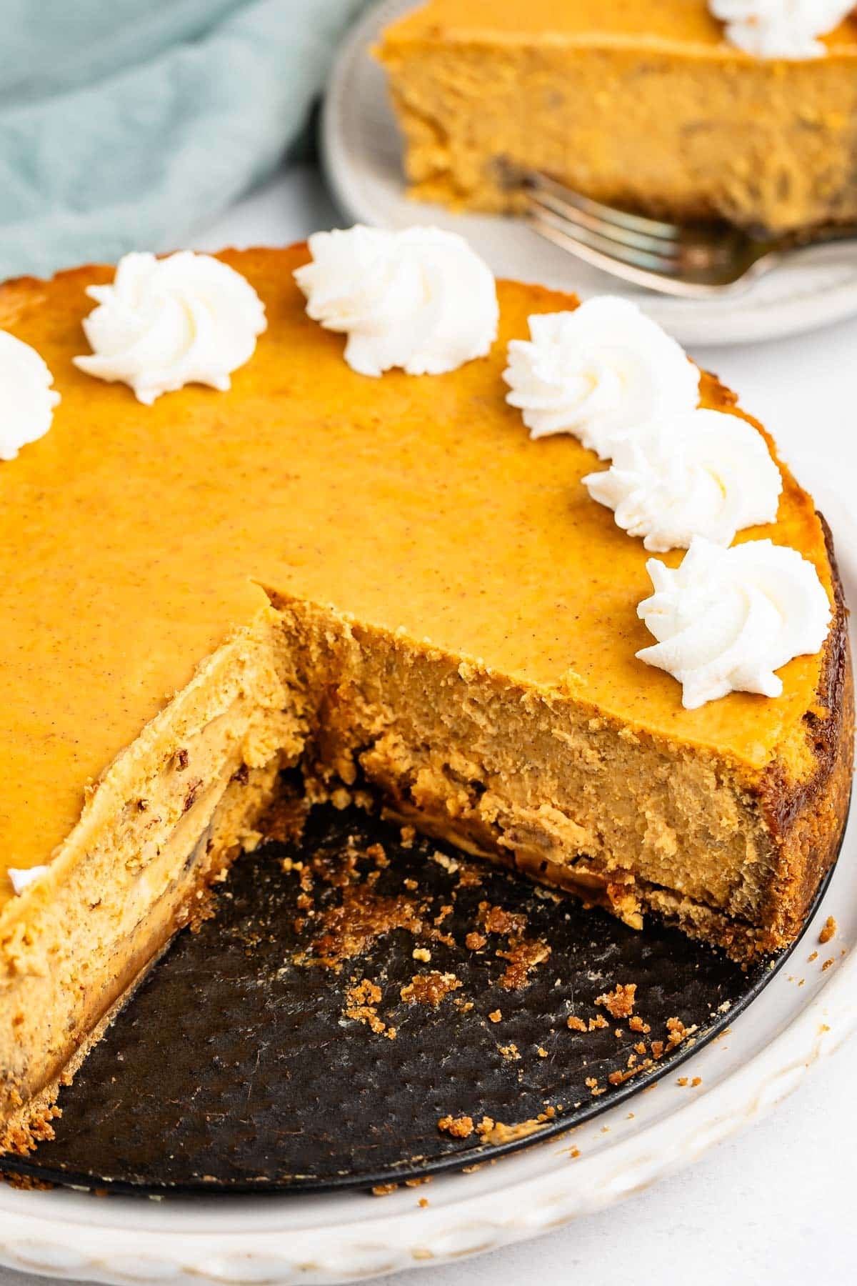 A pumpkin cheesecake with a missing slice, topped with swirls of whipped cream on a plate.