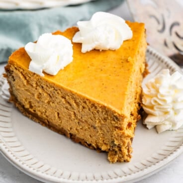 A slice of pumpkin cheesecake on a small plate, topped with two dollops of whipped cream.