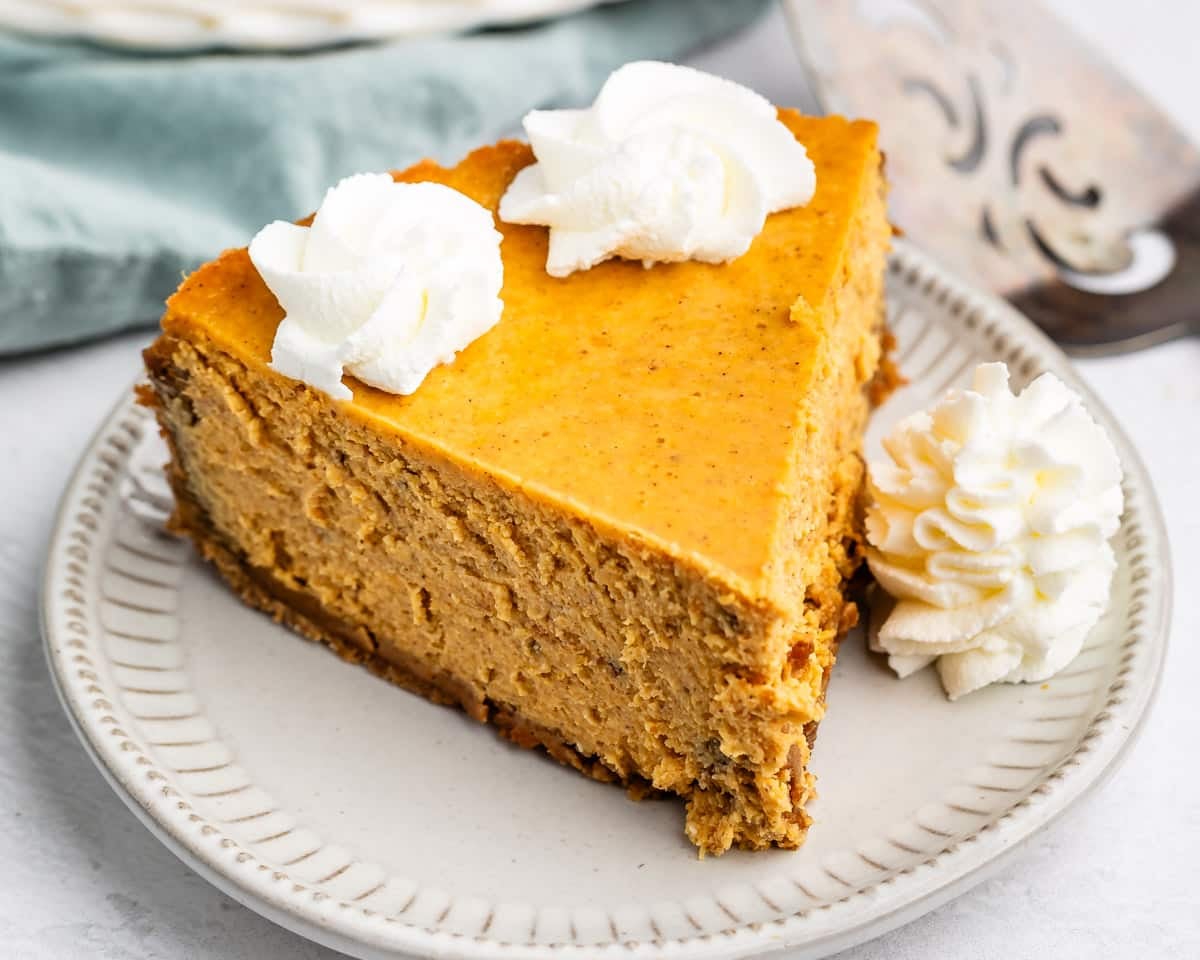 A slice of pumpkin cheesecake on a small plate, topped with two dollops of whipped cream.